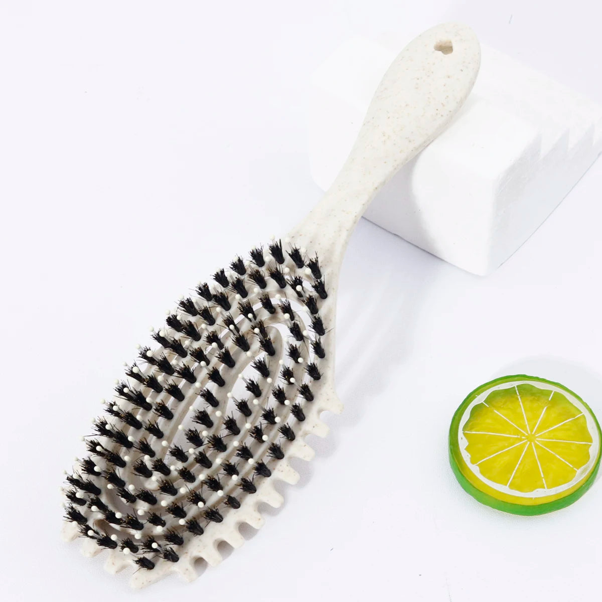 A white bristle hollow arc styling comb resting on a white surface next to a slice of lime.