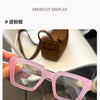 Lunettes de lecture à monture carrée rose rétro sur une surface blanche.