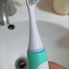 A white electric toothbrush handle with a light blue brush head is held in a hand against a white surface.