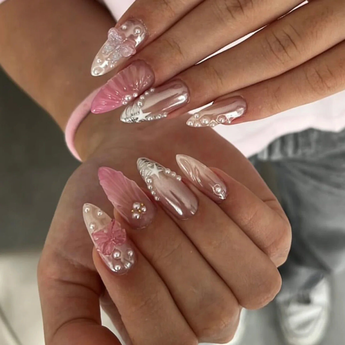 A hand displays a set of 24 press-on nails featuring pink and iridescent floral and butterfly designs.