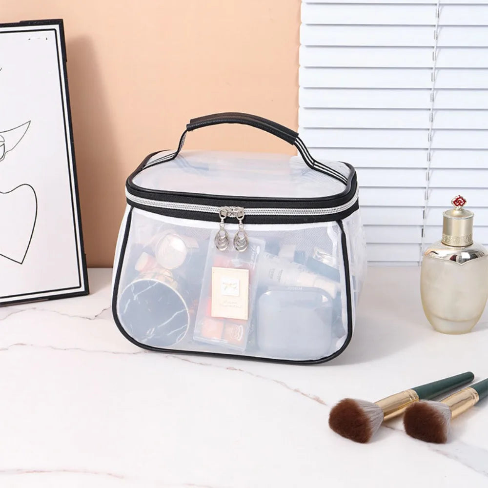 A clear cosmetic bag with a black zipper and handle sits on a white surface next to a silver perfume bottle.
