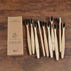 A set of ten natural bamboo toothbrushes packaged in a cardboard box on a wooden surface.