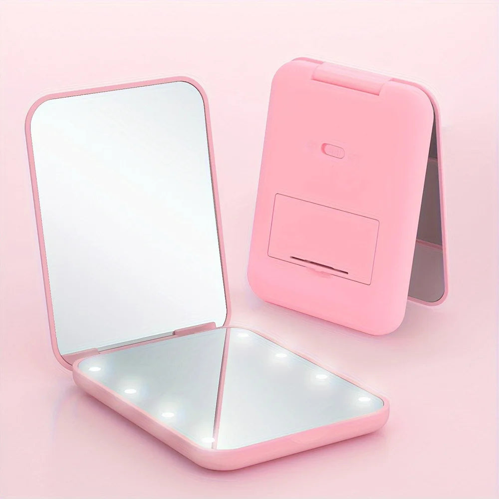 A pink foldable compact LED makeup mirror with a reflective surface and light is shown on a light pink background.