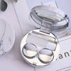 Silver round contact lens storage box with a marble pattern on the lid and clear compartments.