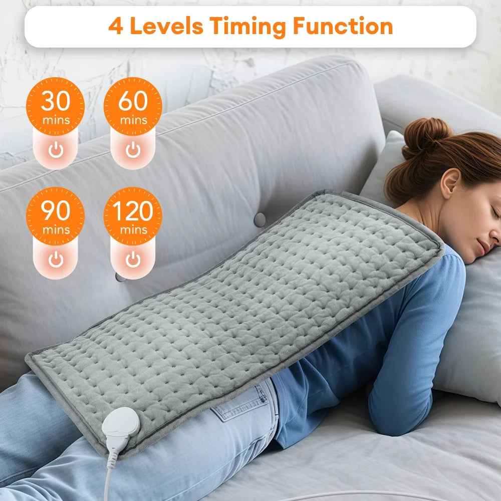 A gray electric heating pad is shown being used on a person's shoulder while lying in bed.