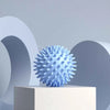 A light blue, textured deep tissue massage ball resting on a white pedestal against a gray background.