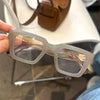 Une paire de lunettes de lecture carrées rétro transparentes avec des verres teintés d'orange, posées sur une surface blanche