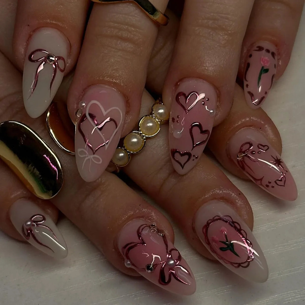 A set of pink heart pearl press-on fake nails displayed on fingers.