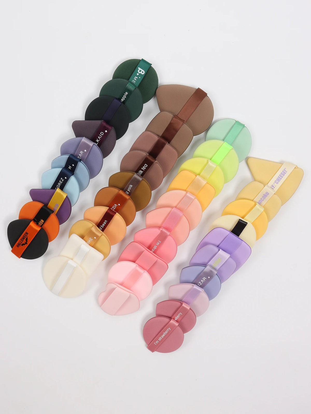 A set of 12 air cushion beauty puffs in various shades of green, brown, and pink arranged diagonally.