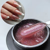 Une main présente un produit de vernis à ongles dans un contenant argenté avec une finition scintillante rose.