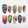 Colección de 10 uñas postizas brillantes con tonos verdes, rosas y negros con diseños florales y mariquitas.