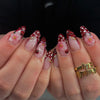 Close-up of hands displaying long almond shaped press-on false nails decorated with red polka dots and ladybug accents
