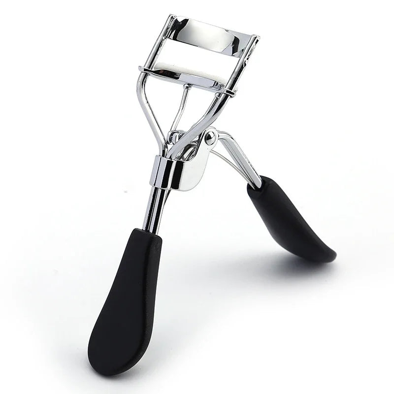 A silver professional eyelash curler with black rubber grips shown against a white background.