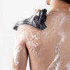 A person's back is being exfoliated with a black loofah and white foam.