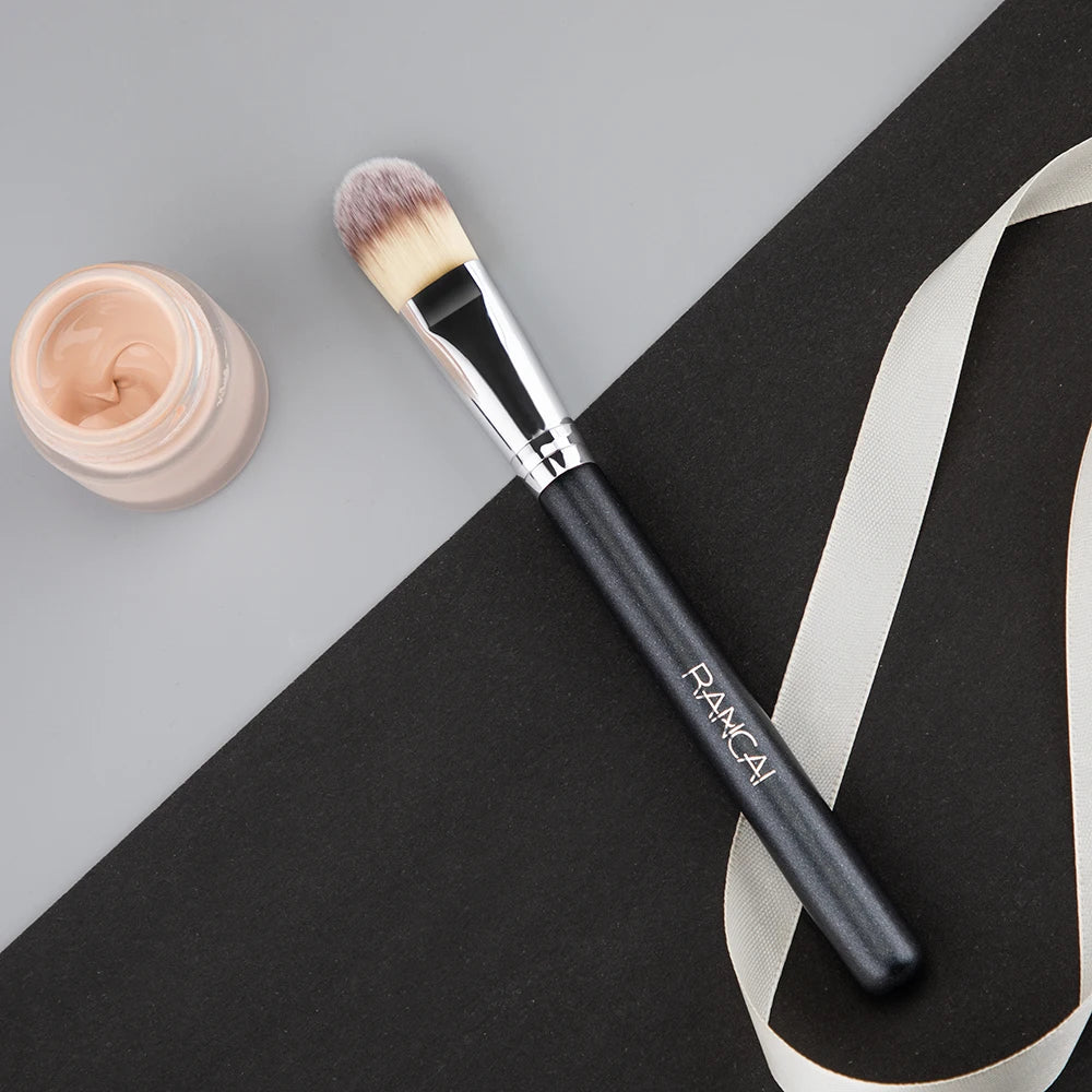 A flat top kabuki foundation brush with a pink-toned bristles rests on a black surface.