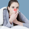 A woman is using a portable infrared nasal therapy device on her nose while wrapped in a white blanket.