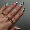 A hand displaying press-on false nails featuring black and white polka dots and ladybugs on an almond shaped nail.