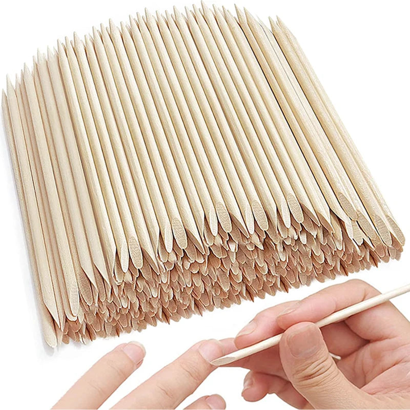 A hand holds a bundle of natural wood nail art pusher sticks.