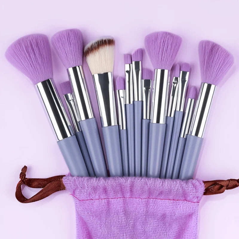 A set of purple makeup brushes with synthetic bristles and silver ferrules resting on a purple cloth.