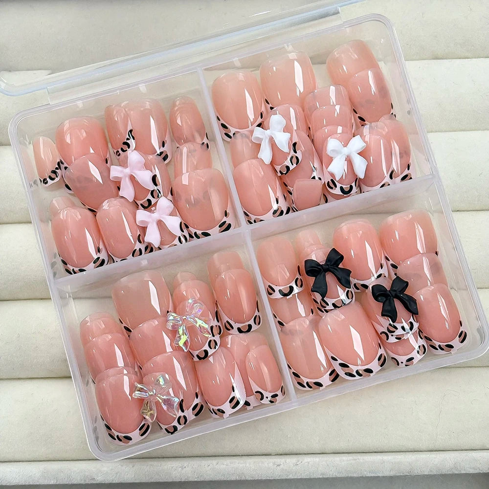 A clear plastic container holds a set of pink press-on nails with black leopard print accents.