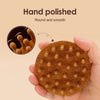 A hand holds a round wooden massage comb with numerous rounded bumps, showing a hand-polished texture.