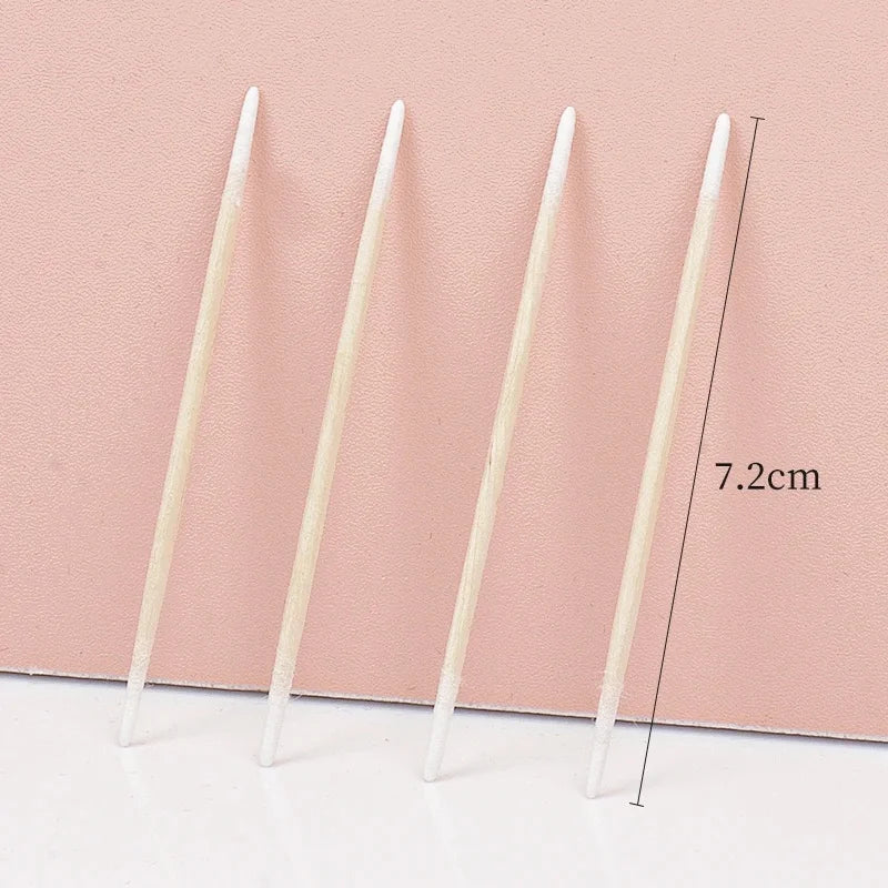 Cinq cotons-tiges blancs jetables disposés sur un fond rose avec une ligne de mesure.