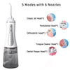 A white portable water flosser device with a clear bottle and six different sized nozzles for various dental cleaning modes.