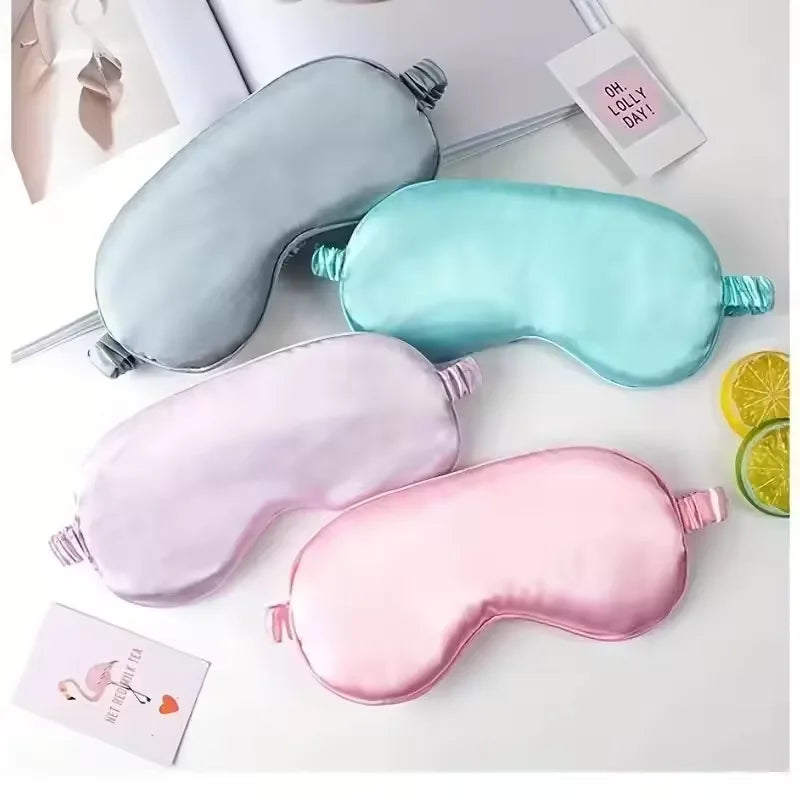 Three double-sided silk eye masks in light blue, mint green, and pink are displayed on a white surface.