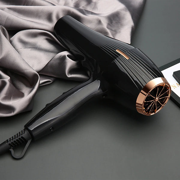 Sèche-cheveux professionnel noir avec une touche rose gold, posé sur une surface de tissu gris.
