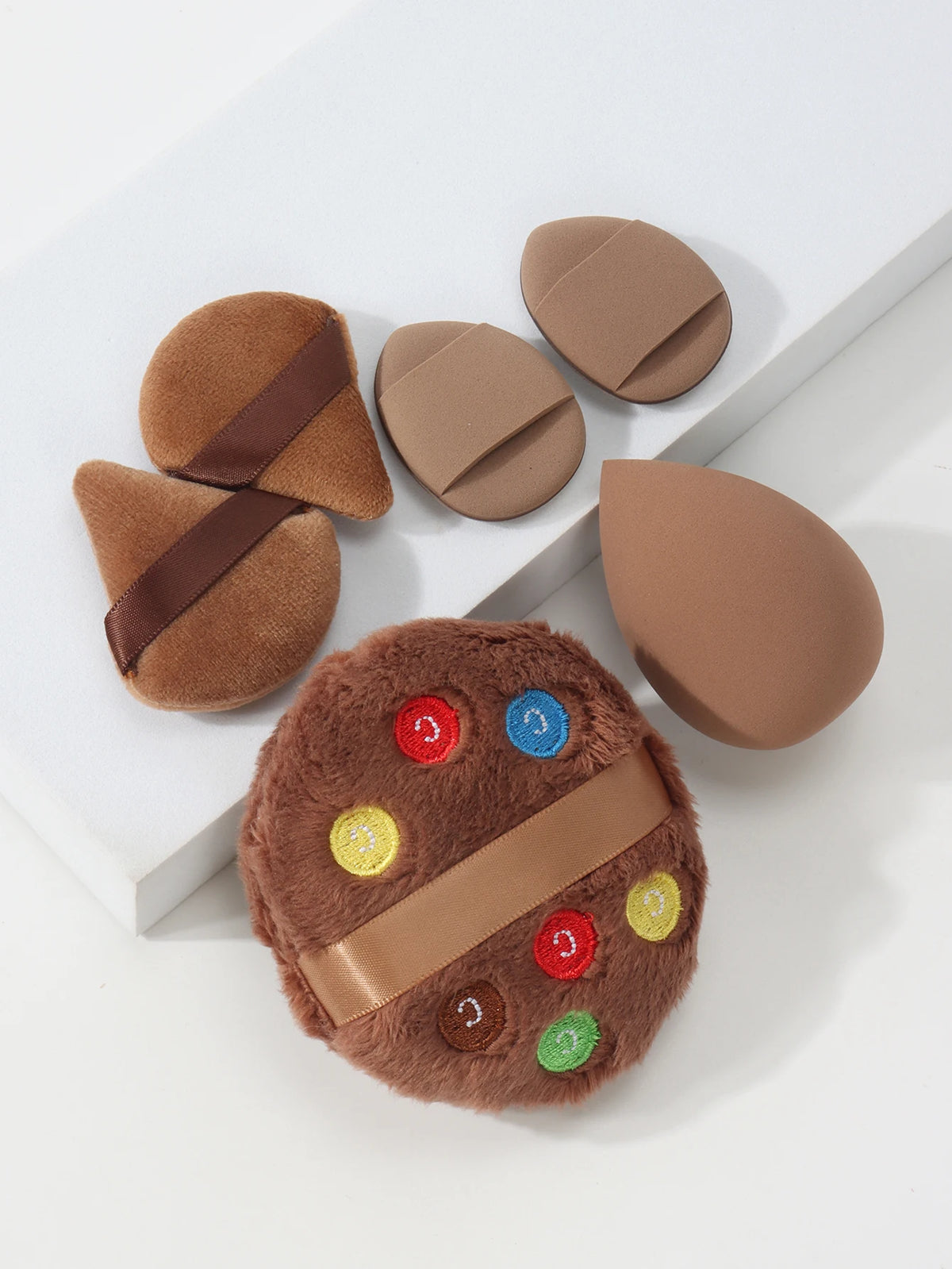 Un ensemble de six poudres légères rondes beige avec des accents marrons, disposées sur une surface blanche.