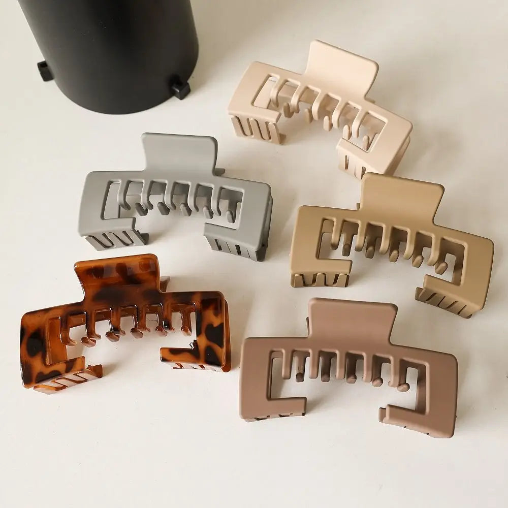 A collection of non-slip hat claw clips in various matte colors and finishes arranged on a white surface.