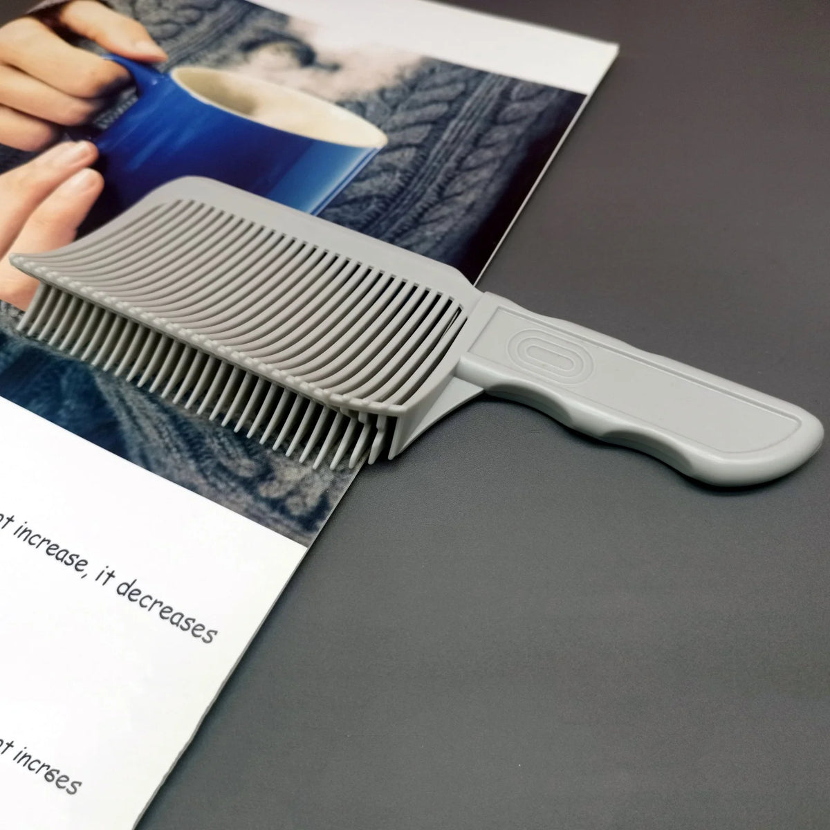 A gray professional barber hair cutting comb is shown next to a magazine featuring a blue cup and natural textures.