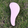 A pink classic detangling hair brush lying on green grass.