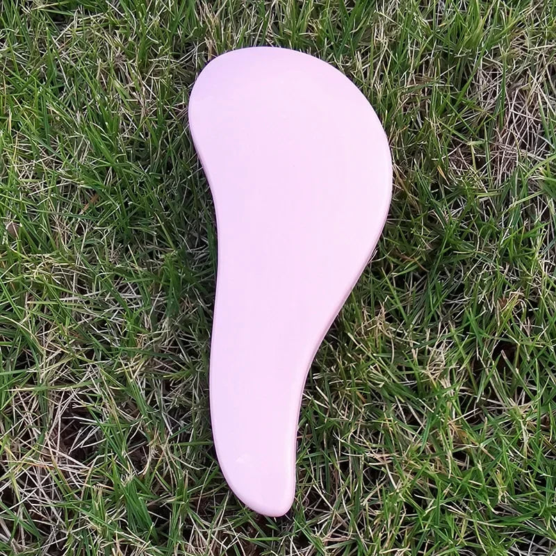A pink classic detangling hair brush lying on green grass.