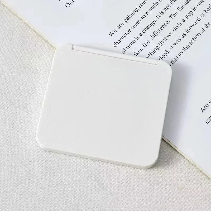 A white double-sided portable makeup mirror resting on a sheet of paper.