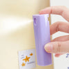 Eine Hand hält eine lila, wiederbefüllbare Sprühflasche vor einer hellen Wand.