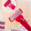 A pink precision safety razor with a replaceable blade is shown, highlighting the blade mechanism.
