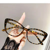 A hand is holding a pair of black and yellow patterned cat eye reading glasses against a light gray background.