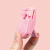 A hand holds a pink mini folding eyelash curler set against a light background.
