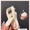 Une main tient un petit recourbe-cils en silicone pour chats, de couleur rose pâle.