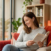 A woman is reading a book while sitting comfortably indoors near a window.