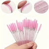 A hand holds a bundle of pink and black disposable eyelash and eyebrow makeup brushes.