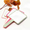 Miroir de maquillage portable compact avec cadre vert clair et accents roses, à côté de feuilles d'automne.