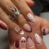 Close-up of a hand displaying press-on false nails with pink and red polka dots and ladybug designs on an almond shape.