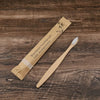 A bamboo toothbrush packaged in kraft paper with a wooden handle and bamboo leaves printed on it.