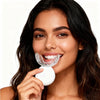 A woman is using a white U-shaped rechargeable teeth whitening kit for cosmetic dental treatment.