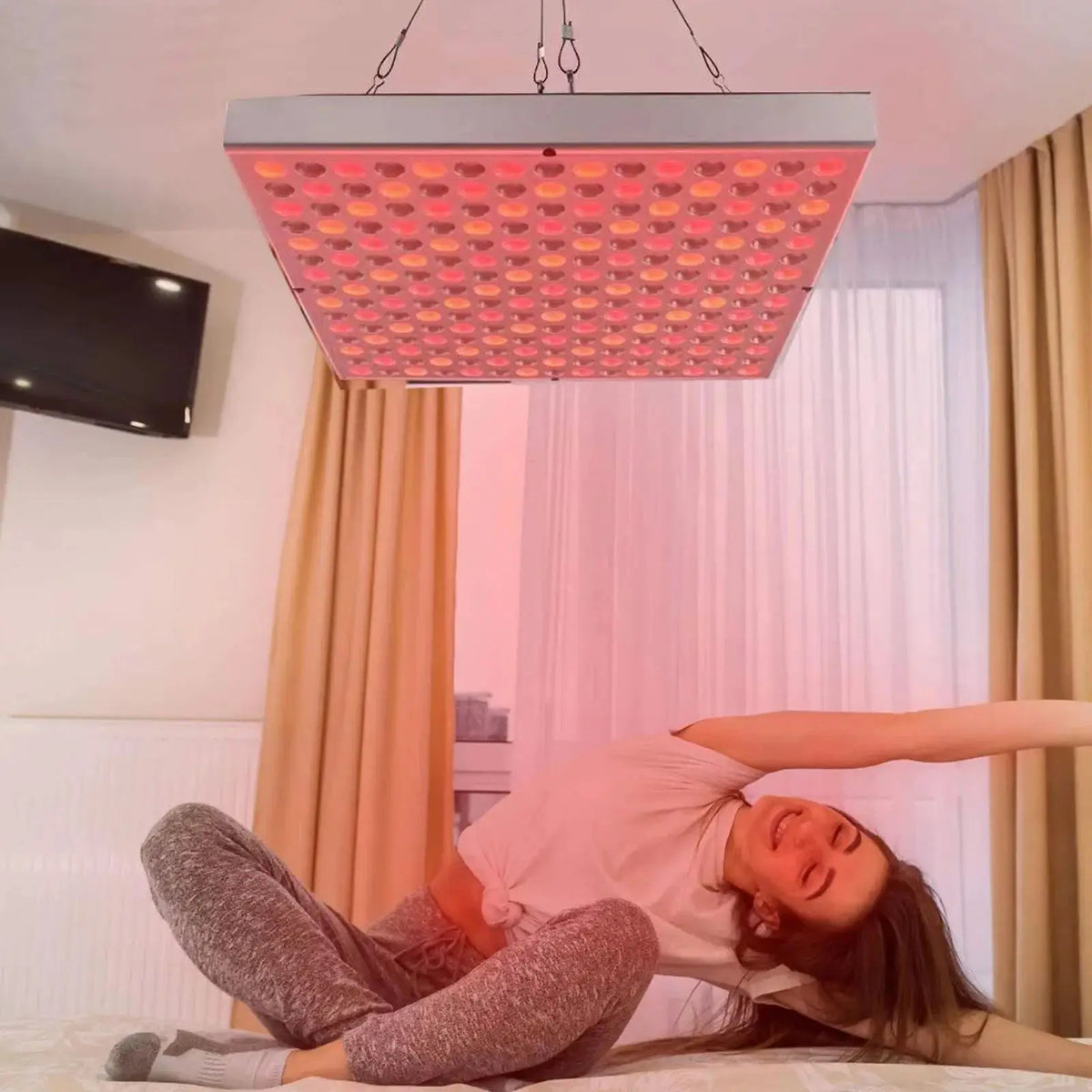 Una persona tumbada bajo un panel de fototerapia LED rojo iluminando su cara y parte superior del cuerpo.