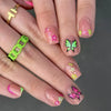 A close-up of a hand displaying various press-on acrylic flower nails with pink, green, and purple accents.