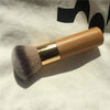 A bamboo airbrush foundation and bronzer brush with a wooden handle and gold ferrule resting on a white cloth.