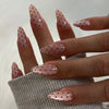 Close-up of fingers displaying pink nails with small glitter dots and an almond shape on a gray sweater.